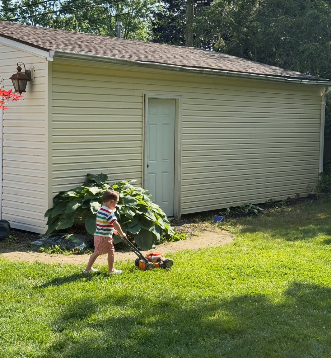 Child pushing a toy mower across a sunny lawn